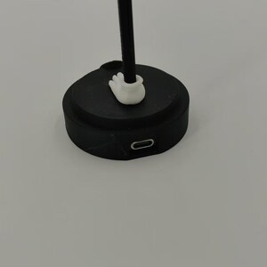 May include: A black charging base with a white plastic connector on top and a USB-C port on the side.