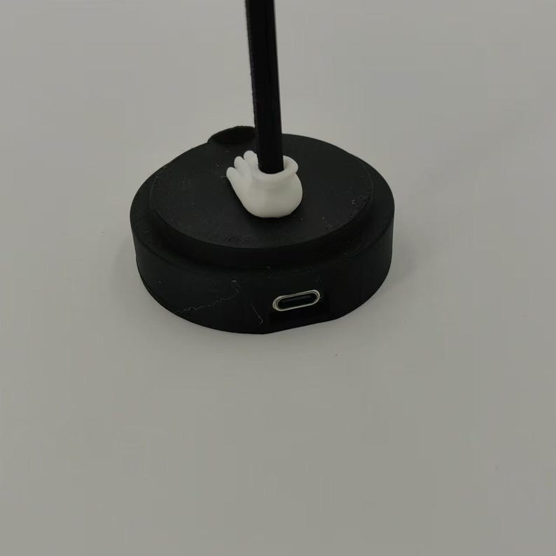 May include: A black charging base with a white plastic connector on top and a USB-C port on the side.