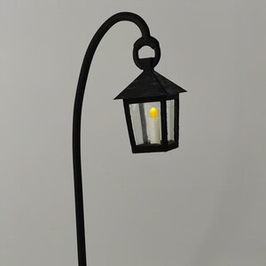 May include: A black metal lamp post with a curved arm and a black lantern with a clear glass panel and a lit candle inside.