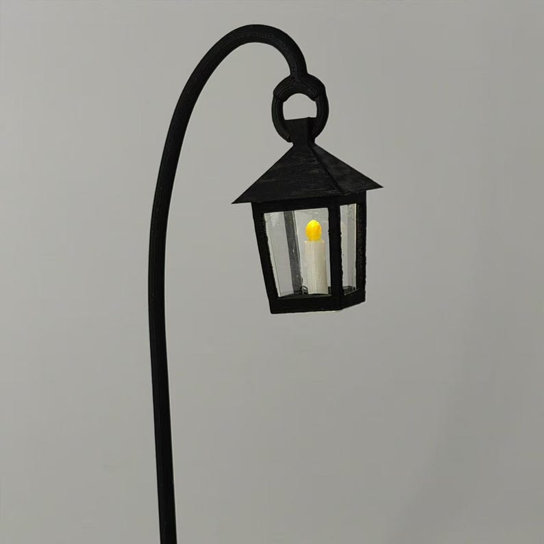 May include: A black metal lamp post with a curved arm and a black lantern with a clear glass panel and a lit candle inside.