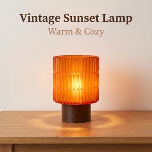 May include: A cylindrical lamp with a ribbed amber glass shade and a dark brown base. The text "Vintage Sunset Lamp" and "Warm & Cozy" appears above the lamp. The glass features a vertical textured pattern that glows with a warm light.
