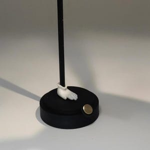 May include: A black and white figurine with a white hand and a black base. The base has a gold metal disc on the side.