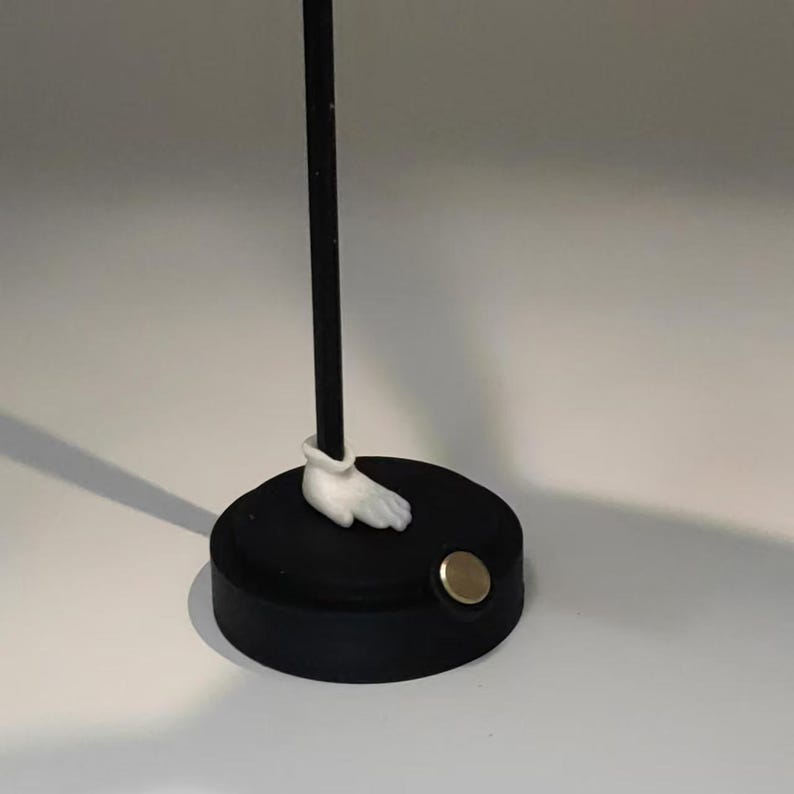 May include: A black and white figurine with a white hand and a black base. The base has a gold metal disc on the side.