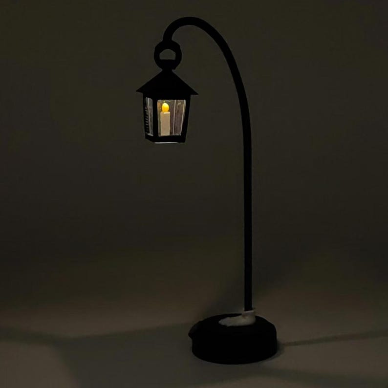 May include: A black metal lamp with a curved arm and a lantern-style shade. The lantern has a clear glass panel and a warm white light inside.