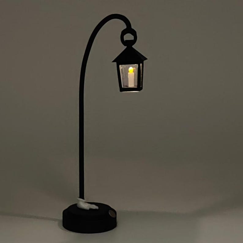 May include: A black metal lamp with a curved arm and a lantern-style light fixture. The lantern has a clear glass panel and a warm white LED light inside.