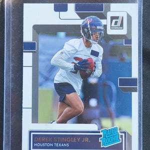 May include: A Derek Stingley Jr. Houston Texans football card. The card features a player in a white uniform and blue helmet, holding a football. The card has the Donruss logo and "Rated Rookie" text.