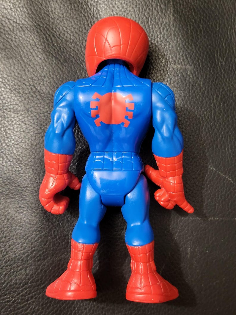 May include: A blue and red Spider-Man action figure. The figure has a red helmet, red gloves, and red boots. The back of the figure has a red spider emblem. The figure is posed with its arms at its sides.