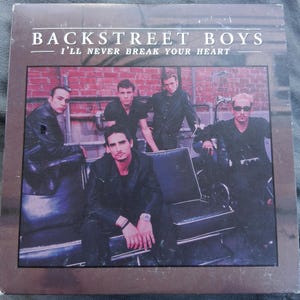 Puede incluir: Una portada de CD de música cuadrada con los Backstreet Boys. El texto dice BACKSTREET BOYS y I'LL NEVER BREAK YOUR HEART. Cinco personas con ropa negra están frente a una pared de ladrillo rojo con tuberías de metal visibles.