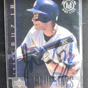 Puede incluir: Una tarjeta de béisbol con Jose Cruz Jr. con el uniforme de los Blue Jays de Toronto, sosteniendo un bate. La tarjeta tiene un diseño azul y plateado con el texto "Upper Deck" y "Hot List". La tarjeta está en una funda protectora.