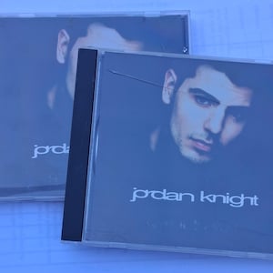 Puede incluir: Dos estuches de CD con un retrato de Jordan Knight sobre un fondo oscuro. El nombre del artista, "jordan knight", está impreso en blanco en la parte inferior del estuche. Los estuches son de plástico transparente.