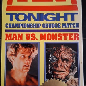 May include: VHS tape for the movie "Arena". The cover features the title in red and the tagline "Tonight Championship Grudge Match Man vs. Monster". Images of a man and a monster are displayed. A gold sticker reads "New Release".