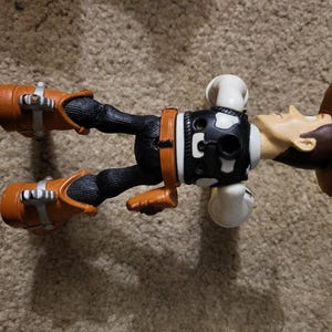 Op de afbeelding: Een plastic action figure van Woody uit de Toy Story-franchise. Woody draagt zijn kenmerkende bruine cowboyhoed, vest en laarzen. Hij ligt op zijn rug met zijn armen gestrekt.