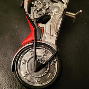 May include: A black and red motorcycle figurine with a silver engine and wheels. The motorcycle has a Budweiser logo on the side and stars on the wheels.
