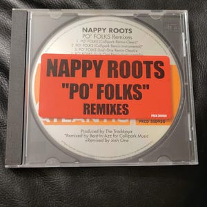 May include: A CD case featuring the album "Po' Folks Remixes" by Nappy Roots. The CD label is visible through the clear case, with a prominent orange sticker displaying the album title and artist name in bold black text.