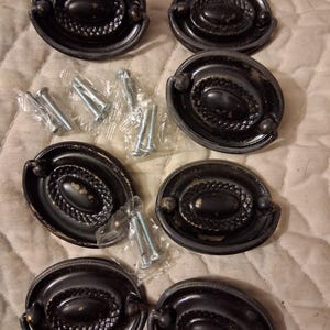 May include: Set of six antique-style black oval drawer pulls with decorative detailing. Each pull has a central oval design and two small knobs. Includes silver screws for installation. Ideal for furniture restoration or DIY projects.
