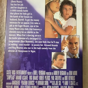 May include: A VHS tape for the film "Striptease" featuring Demi Moore. The cover art includes images of the actors and the film's title, "Demi is dynamite." The back of the tape includes a synopsis and credits.