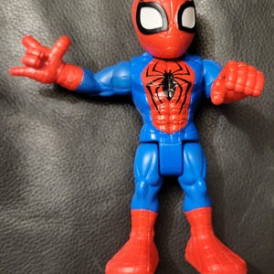 May include: A Spider-Man action figure in a dynamic pose. The figure features a red and blue color scheme, with a red mask and boots, and a blue torso and legs. The Spider-Man logo is prominently displayed on the chest.