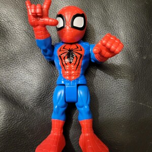 May include: A Spider-Man action figure in a dynamic pose. The figure features a red and blue color scheme, with a red mask and spider emblem on the chest. The figure's hand is raised in a gesture.