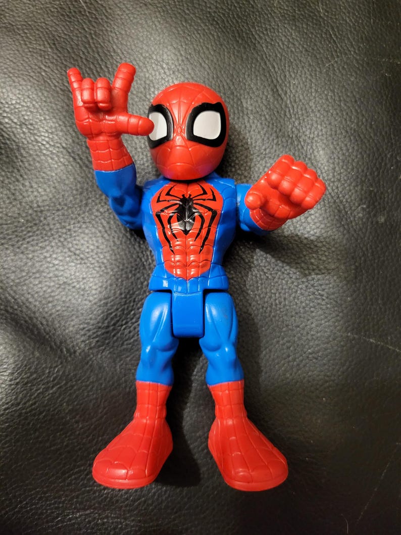 May include: A Spider-Man action figure in a dynamic pose. The figure features a red and blue color scheme, with a red mask and spider emblem on the chest. The figure's hand is raised in a gesture.