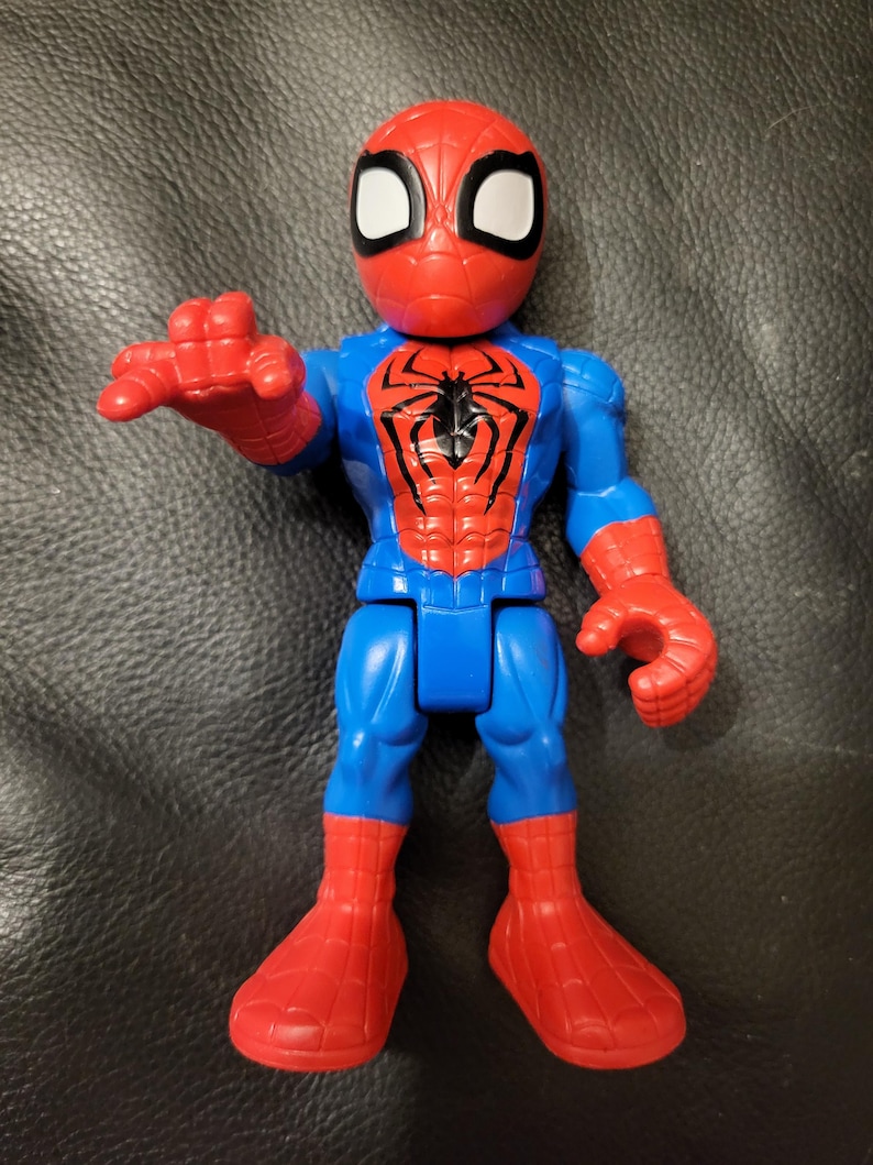 May include: A plastic Spider-Man action figure in a classic pose. The figure features a red mask with white eye lenses, a blue torso and legs, and red hands and feet. A black spider emblem is on the chest.