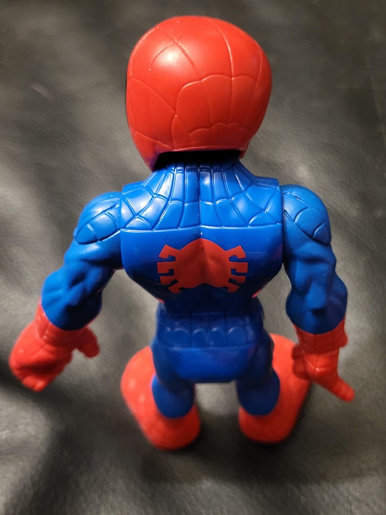 May include: A plastic Spider-Man action figure, viewed from the back. The figure is primarily blue with red accents on the head, hands, and feet. A red spider emblem is on the back. The figure is kneeling.