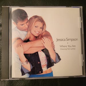 May include: A CD case featuring Jessica Simpson and Nick Lachey. The album cover displays a photo of the two embracing. The text on the cover reads "Jessica Simpson Where You Are (Featuring Nick Lachey)". The CD case is clear with a black spine.