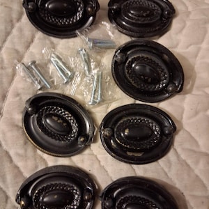 May include: Six oval black drawer pulls with a rope-like border and central oval design. Screws are included. The pulls have a vintage or antique appearance. Each pull is approximately 10 cm in length.