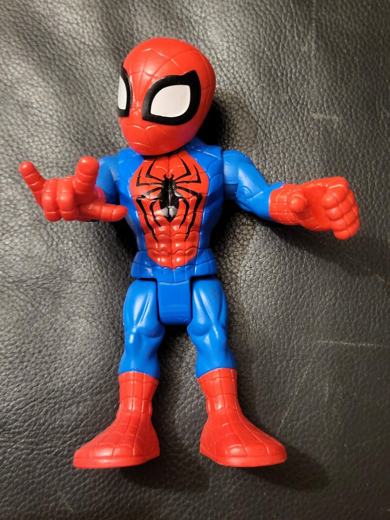 May include: A Spider-Man action figure with a red head and boots, blue torso and arms, and a red chest. The figure has a black spider emblem on the chest and white eye shapes.