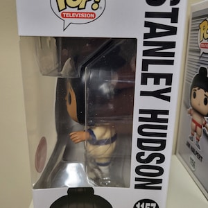 May include: A Funko Pop! Television vinyl figure of Stanley Hudson from The Office. The figure is wearing a white and blue uniform with a black hair bun. The box is white with black text that reads "Stanley Hudson" and "Pop! Television". The number 1157 is printed on the box.
