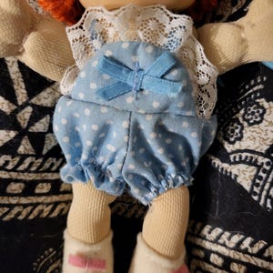 May include: A vintage doll with orange yarn hair, a fair complexion, and a blue polka-dot romper with a matching bow. The doll is wearing white shoes with pink bows and a white lace collar.