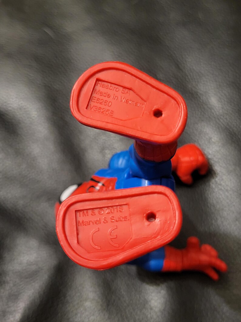 May include: A Spider-Man action figure in a crouching position, viewed from below. The figure is primarily blue and red, with red feet and hands. The soles of the feet are red and bear the Hasbro SA and Marvel & Subs. markings.