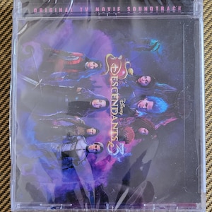 May include: A purple and gold CD case with the text "Disney Descendants 3" and "Original TV Movie Soundtrack" on the front. The case features a group of characters from the movie, including Mal, Evie, Carlos, Jay, and Uma.