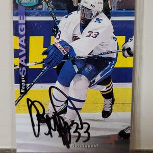 May include: A hockey trading card featuring Reggie Savage of the Nordiques, wearing a white and blue uniform with the number 33. The card has an autograph and the Parkhurst logo. The background shows the ice rink.
