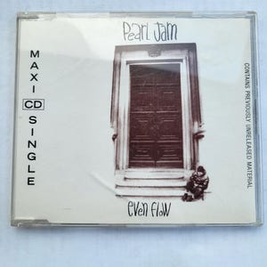 May include: A CD single case featuring the Pearl Jam album "Even Flow." The cover art depicts a sepia-toned image of a doorway with a person sitting on the steps. The text "Pearl Jam," "MAXI-SINGLE," and "Even Flow" are visible.