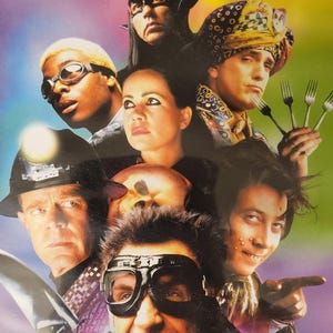 Peut inclure: Couverture de DVD avec un groupe de personnes aux expressions et tenues variées. Le mot "MEN" est en haut. L'image a un fond coloré avec un dégradé violet et vert.