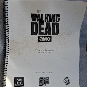 以下が含まれることがあります： AMC、Play Mechanix、Raw Thrillsによるアーケードゲーム「The Walking Dead」の白いスパイラル綴じサービスマニュアル。表紙には黒い文字でゲームタイトル、セットアップおよび操作手順、2016年の著作権情報が記載されています。