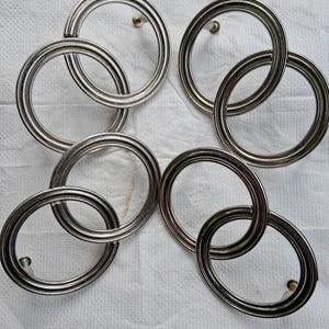 Puede incluir: Un juego de cuatro tiradores de armario circulares de metal plateado. Cada tirador presenta un diseño de doble anillo con un acabado liso y pulido, y un poste de montaje central visible en la parte posterior.