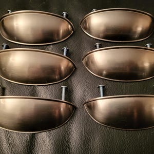 May include: Six brushed nickel cabinet pulls with a rounded oval shape. The pulls have a satin finish and are designed for use on cabinets, drawers, and furniture.