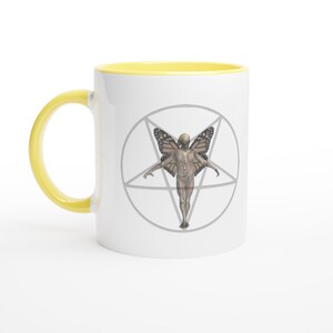 Könnte beinhalten: Weiße Keramiktasse mit gelbem Henkel und Innenraum. Die Tasse zeigt eine detaillierte Illustration einer menschlichen Figur mit Schmetterlingsflügeln in einem grauen Pentagramm. Das Design ist auf der Oberfläche der Tasse zentriert.