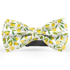 May include: A white bow tie with a lemon print. The bow tie features yellow lemons with green leaves and white flowers on a white background.