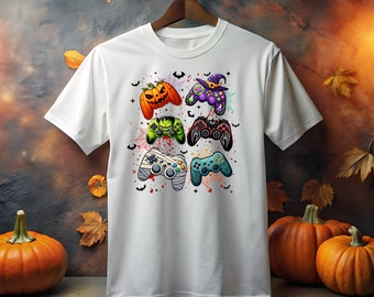 以下が含まれることがあります： ハロウィンをテーマにしたビデオゲームコントローラー5つのグラフィックが描かれた白いTシャツ。コントローラーは、カボチャ、コウモリ、その他の不気味な要素で飾られています。