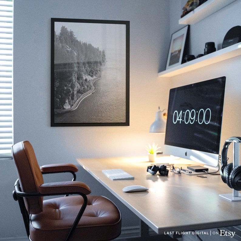 May include: A home office workspace with a desk, chair, computer, and a framed black and white photograph of a coastline. The computer screen displays the time 04:09:00.