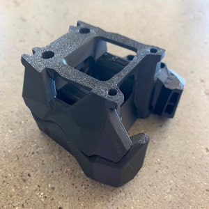 May include: A black 3D printed object with a rectangular shape and a series of holes and openings. The object is made of a textured material and has a complex design.