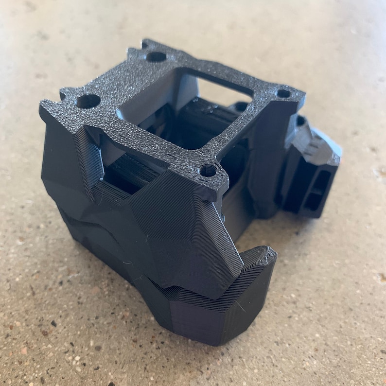 May include: A black 3D printed object with a rectangular shape and a series of holes and openings. The object is made of a textured material and has a complex design.
