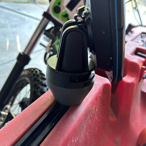 May include: A black and gray fish finder mount with a swivel joint, attached to a red kayak.