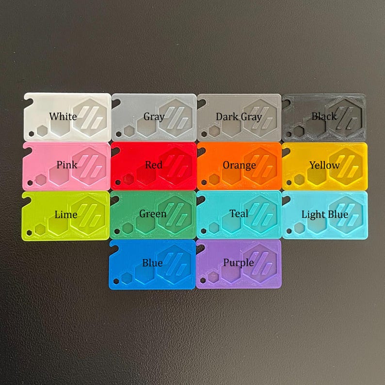 May include: A set of 15 plastic keychains in various colors, each with a hexagonal design and the color name printed on it. The colors include white, gray, dark gray, black, pink, red, orange, yellow, lime, green, teal, light blue, blue, and purple.