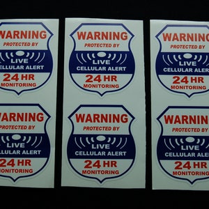 May include: Six white stickers with blue and red text. Each sticker has a shield shape and reads "WARNING PROTECTED BY LIVE CELLULAR ALERT 24 HR MONITORING".