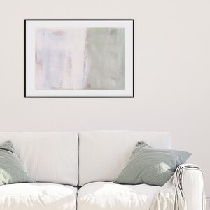 K&ouml;nnte beinhalten: Ein gerahmtes abstraktes Gem&auml;lde in Wei&szlig;- und Gr&uuml;nt&ouml;nen h&auml;ngt an einer wei&szlig;en Wand &uuml;ber einem wei&szlig;en Sofa mit gr&uuml;nen Kissen.