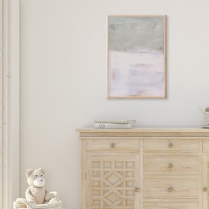 K&ouml;nnte beinhalten: Eine Kommode aus hellem Holz mit sechs Schubladen und einem geschnitzten Design auf der Vorderseite. Die Kommode hat Messingkn&ouml;pfe. Ein gerahmtes abstraktes Gem&auml;lde in hellgr&uuml;nen und rosafarbenen Farben h&auml;ngt an der Wand &uuml;ber der Kommode. Ein Stoffteddyb&auml;r sitzt in einem Weidenkorb vor der Kommode.