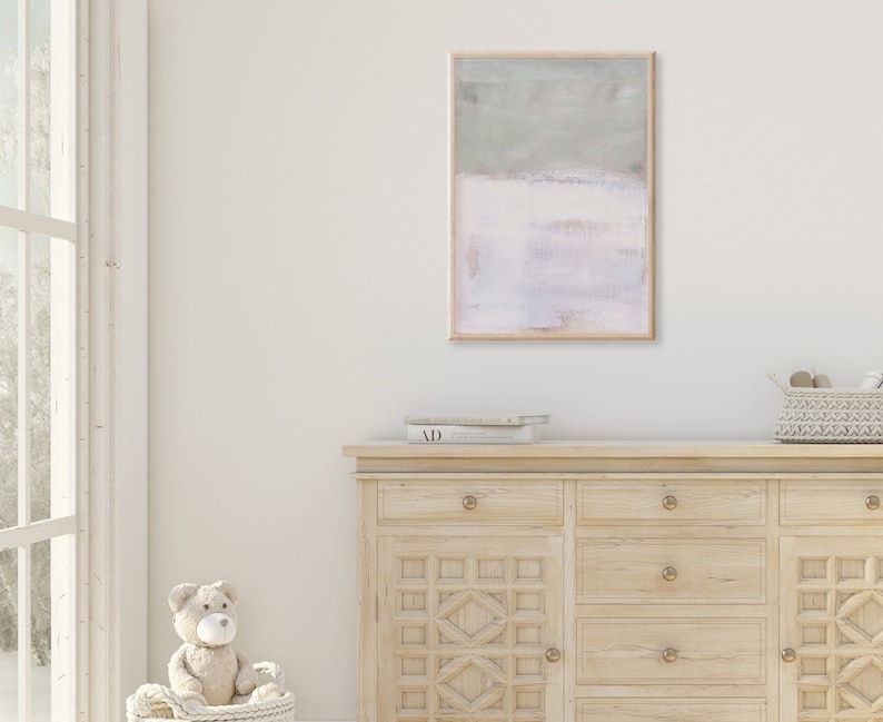 K&ouml;nnte beinhalten: Eine Kommode aus hellem Holz mit sechs Schubladen und einem geschnitzten Design auf der Vorderseite. Die Kommode hat Messingkn&ouml;pfe. Ein gerahmtes abstraktes Gem&auml;lde in hellgr&uuml;nen und rosafarbenen Farben h&auml;ngt an der Wand &uuml;ber der Kommode. Ein Stoffteddyb&auml;r sitzt in einem Weidenkorb vor der Kommode.